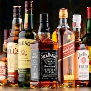 Blog 5 A collection of various alcohol bottles, including whiskey, vodka, and rum, displayed on a wooden shelf.