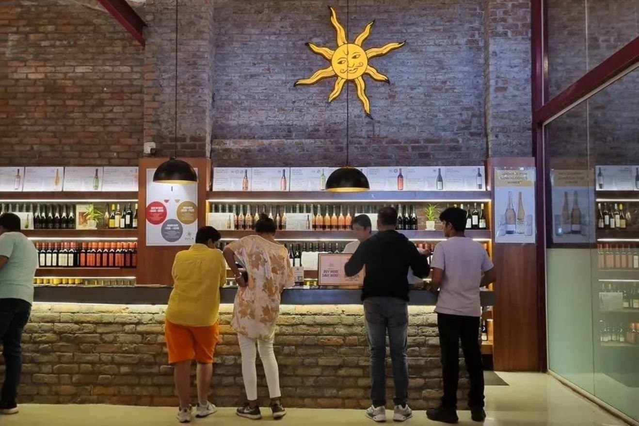 Sula Wines and Nashik: How the Region Became Associated with Indian Wine 26 A group of people socializing in front of a wine bar, showcasing a lively atmosphere and various wine bottles displayed.