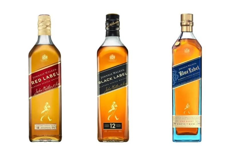 Three bottles of Johnnie Walker whisky: Black Label, Blue Label, and Gold Label, displayed in a row on a wooden surface.
